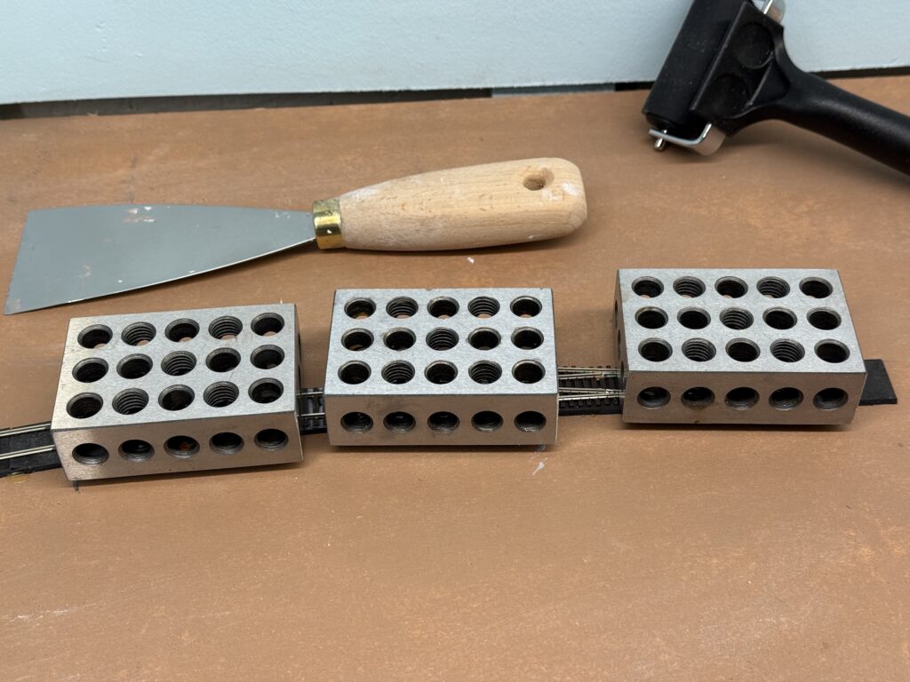 Laying Tracks: holding them in place with metal blocks after glueing.